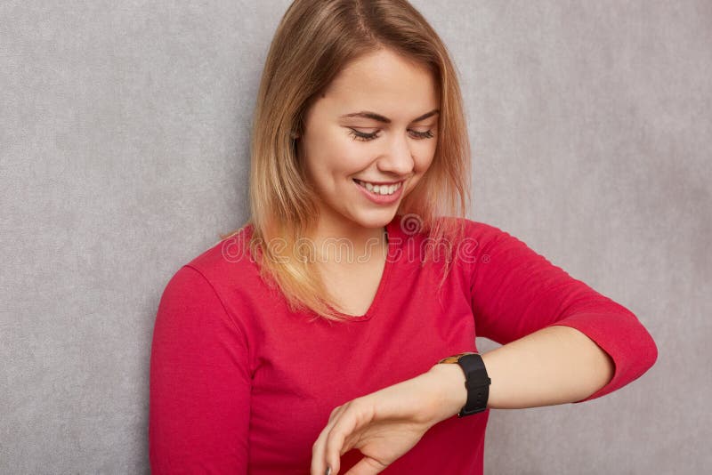 Wizerunek rozochocona blondynki kobieta ubierająca wewnątrz patrzeje pozytywnie przy wristwatch, sprawdza czas, raduje się mieć w fotografia stock Wizerunek rozochocona blondynki kobieta ubierająca wewnątrz patrzeje pozytywnie przy wristwatch, sprawdza czas, raduje się mieć w fotografia stock