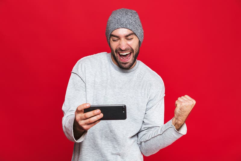 Wizerunek zarośnięty mężczyzny 30s mienia smartphone i bawić się gra wideo nad czerwonym tłem, fotografia stock Wizerunek zarośnięty mężczyzny 30s mienia smartphone i bawić się gra wideo nad czerwonym tłem, fotografia stock