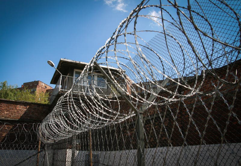 Barbed-wire and brick walls in order to secure prison area. A guardroom in the background. Barbed-wire and brick walls in order to secure prison area. A guardroom in the background.