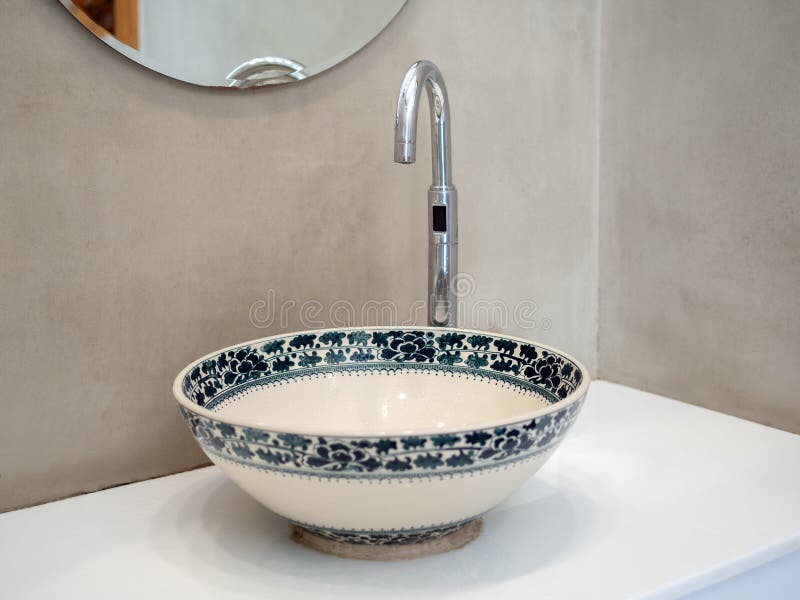 Clean loft style bathroom interior with porcelain sink basin faucet on white marble shelf and round mirror on concrete wall background. Clean loft style bathroom interior with porcelain sink basin faucet on white marble shelf and round mirror on concrete wall background