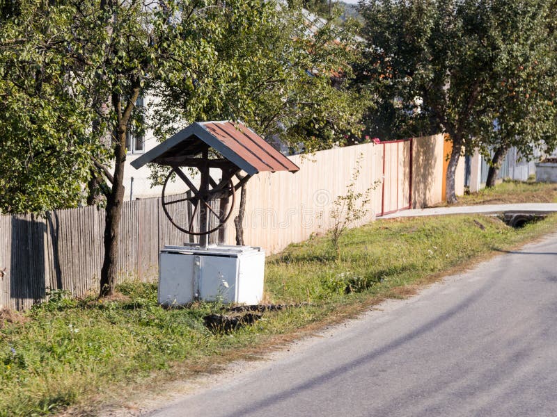 Wodnego well pozycja na wioski ulicie blisko ogrodzenia w Rumunia obraz stock Wodnego well pozycja na wioski ulicie blisko ogrodzenia w Rumunia obraz stock