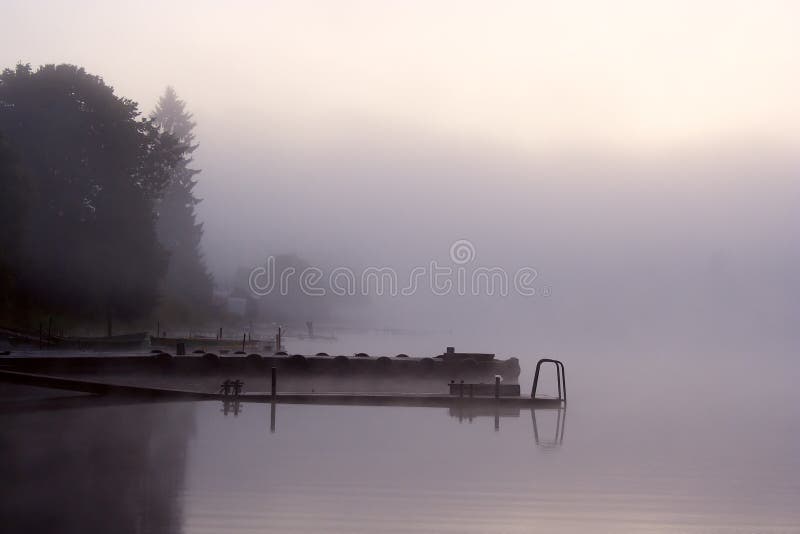 Morning nature scene (landscape): fog (mist) reflected in the water surface along with trees and moorage (quay, berth, wharf). The Seliger lake (Russia). Can be used as a background (backdrop) or wallpaper. Morning nature scene (landscape): fog (mist) reflected in the water surface along with trees and moorage (quay, berth, wharf). The Seliger lake (Russia). Can be used as a background (backdrop) or wallpaper.