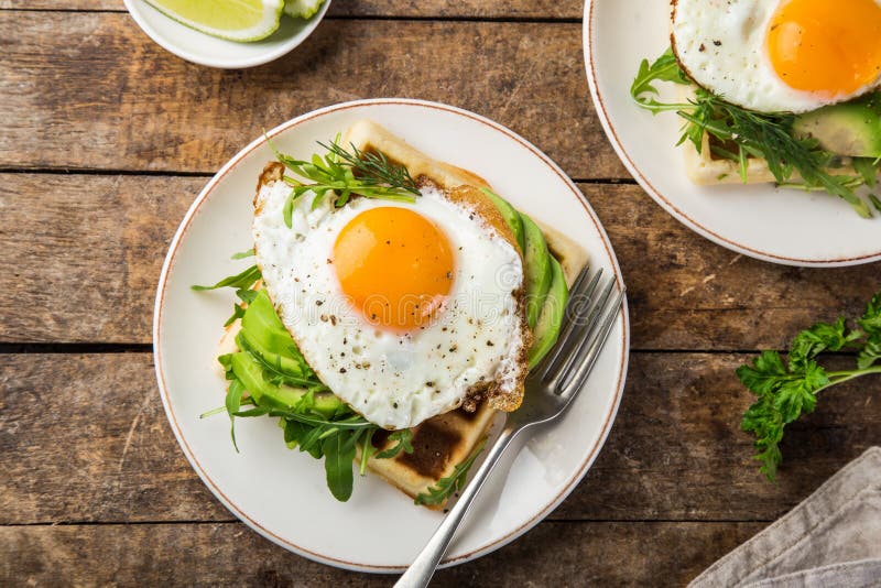 Wohlschmeckende Waffeln mit Avocado, Arugula und Spiegelei zum Frühstück stockfotografie Wohlschmeckende Waffeln mit Avocado, Arugula und Spiegelei zum Frühstück stockfotografie