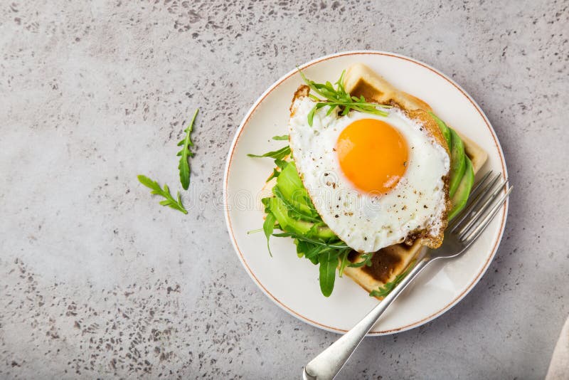 Wohlschmeckende Waffeln mit Avocado, Arugula und Spiegelei zum Frühstück lizenzfreies stockbild Wohlschmeckende Waffeln mit Avocado, Arugula und Spiegelei zum Frühstück lizenzfreies stockbild