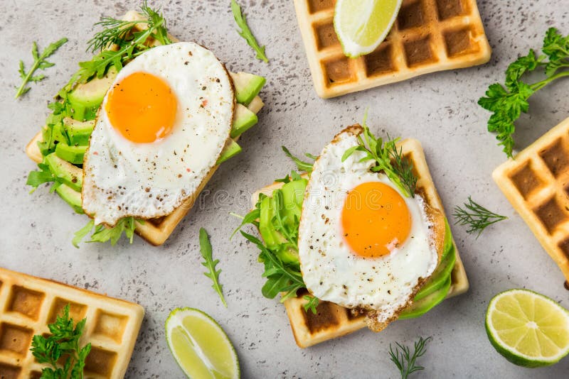 Wohlschmeckende Waffeln mit Avocado, Arugula und Spiegelei zum Frühstück stockbild Wohlschmeckende Waffeln mit Avocado, Arugula und Spiegelei zum Frühstück stockbild
