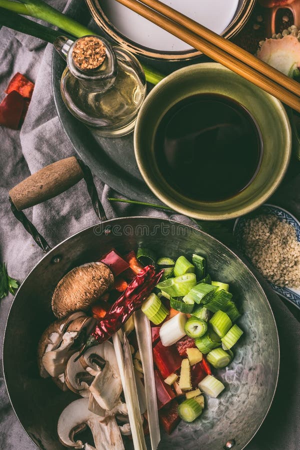Wok mit gehacktem Gemüse und Gewürzen auf Küchentischhintergrund mit Essstäbchen, Sojasoße und Öl des indischen Sesams Asiatische stockfotos