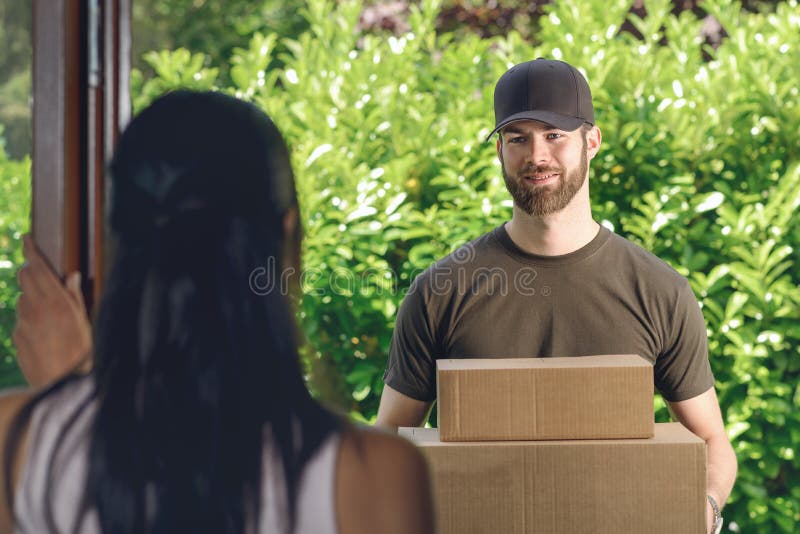 Woman answering the door to an attractive bearded deliveryman carrying two cardboard cartons for delivery, view over her shoulder from behind. Woman answering the door to an attractive bearded deliveryman carrying two cardboard cartons for delivery, view over her shoulder from behind