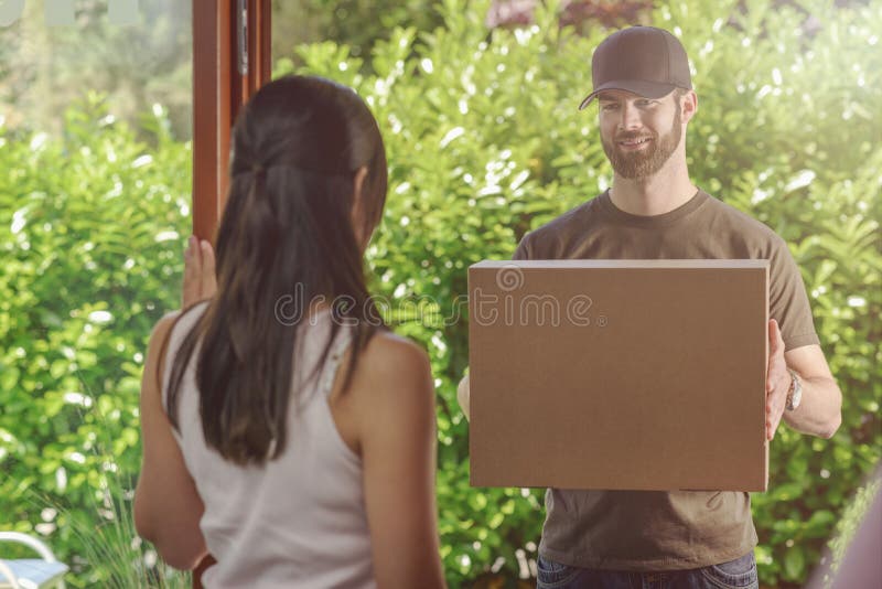 Woman answering the door to an attractive bearded deliveryman carrying two cardboard cartons for delivery, view over her shoulder from behind. Woman answering the door to an attractive bearded deliveryman carrying two cardboard cartons for delivery, view over her shoulder from behind