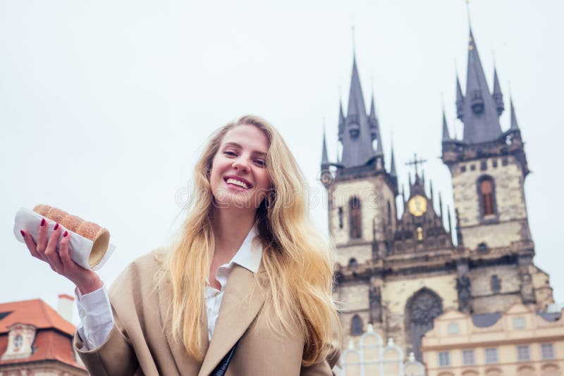 Woman with an appetite eats a traditional Czech sweet Trdelnik in street Prague s Old Town Square