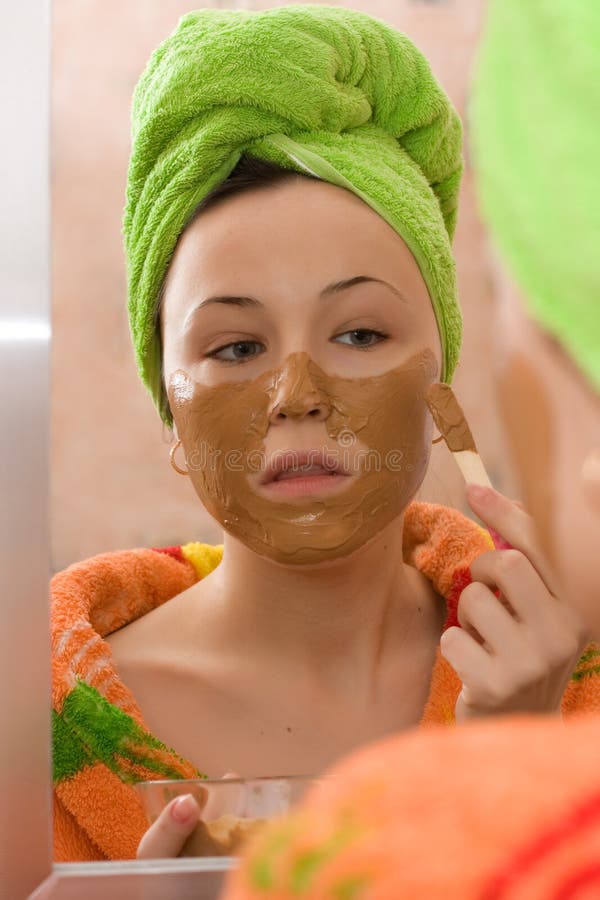 Woman applying facial mask from brown clay