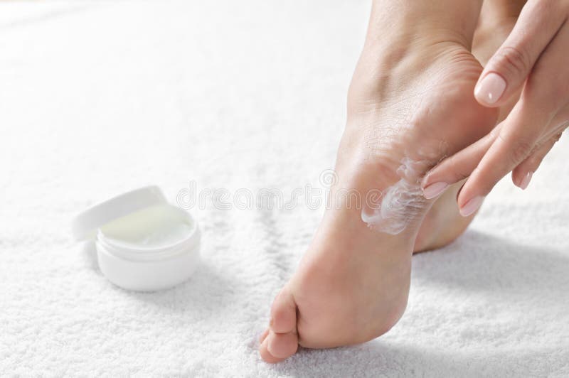 Woman applying foot cream on white towel, closeup. Spa treatment