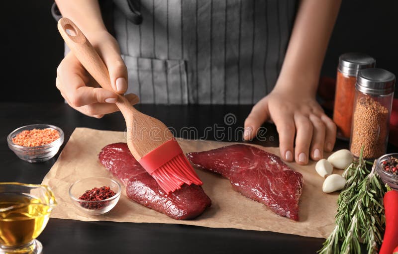 Woman applying oil on raw steak with silicone brush stock photography Woman applying oil on raw steak with silicone brush stock photography