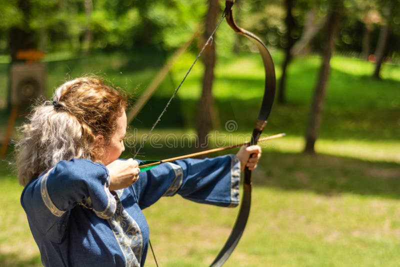Woman archer with bow shoot arrow in the forest on knight festival in a traditional suit stock photography Woman archer with bow shoot arrow in the forest on knight festival in a traditional suit stock photography