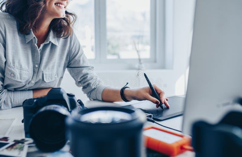 Female photographer working on computer using drawing pad at her desk. Young woman using graphic tablet and drawing pen to retouch the images. Computer editing stock images, royalty-free photos and pictures