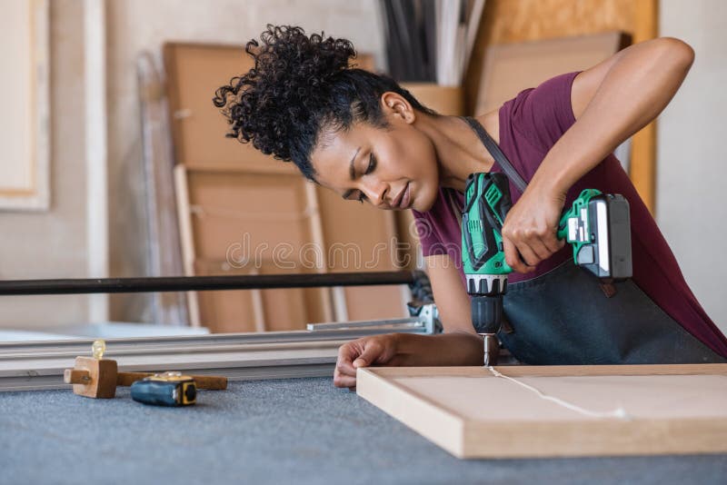 Woman assembling a frame with a drill in her workshop