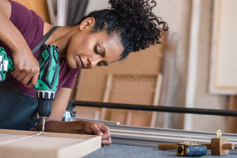 Woman assembling a frame using a drill in her workshop