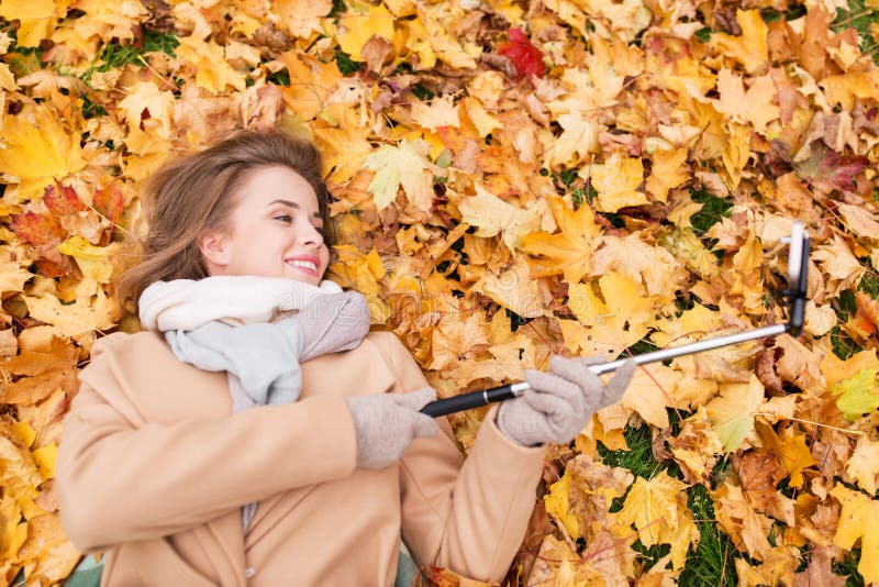 Woman on autumn leaves taking selfie by smartphone