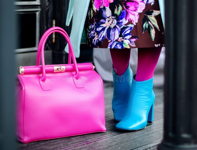 Woman in autumn or spring in a bright coat and a pink big bag. Blue boots, boots. Fashionable bag close-up in female hands.