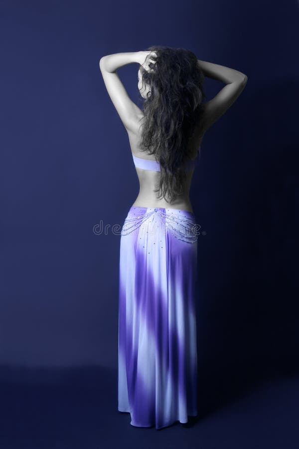 Woman back in blue oriental skirt. Show girl in dancer's dress demonstrated long skirt. Dark blue background. Woman back in blue oriental skirt. Show girl in dancer's dress demonstrated long skirt. Dark blue background.