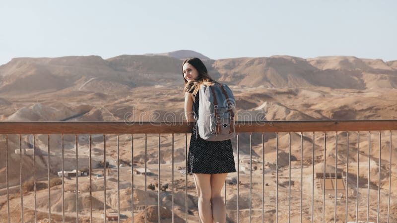 Woman with backpack looks at massive mountain view. Pretty Caucasian girl enjoys incredible desert panorama. Israel 4K.