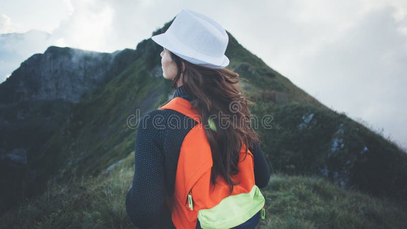 Woman with backpack and white hat traveling along foggy and cloudy mountains