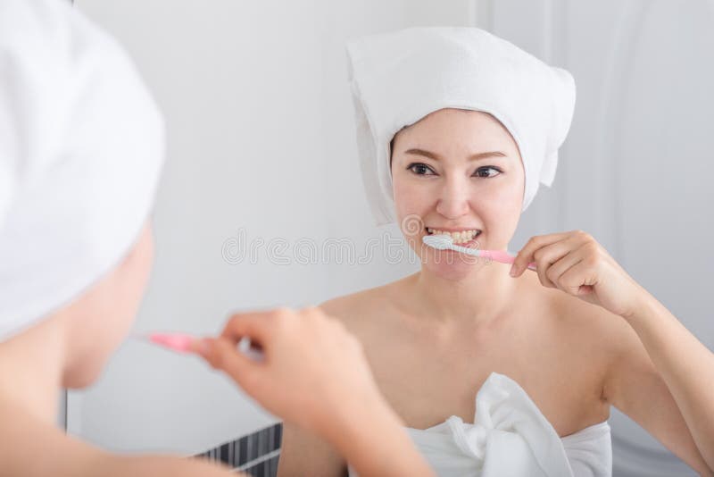 Woman in Bath Towel Brushing Teeth with Mirror in Bathroom Stock Image