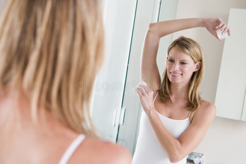 Woman in bathroom applying deodorant smiling