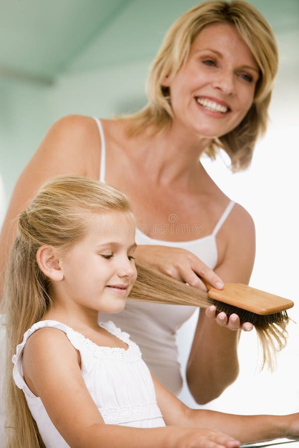 Woman in bathroom brushing young girl's hair smiling