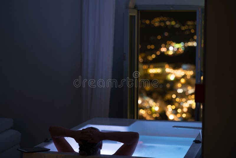 Woman in the bathroom at the hotel enjoying the view of the night city