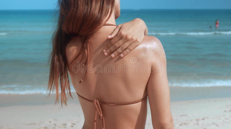 Woman at beach carefully applies sunscreen to shoulder shielding skin from sun damage. Sunscreen fortifies defense