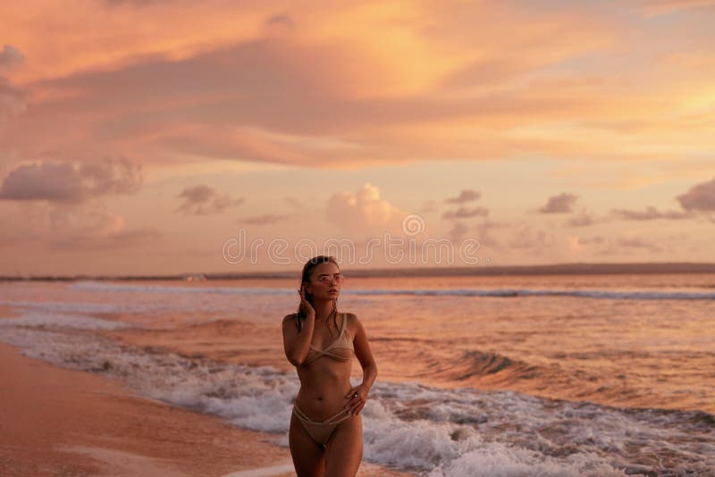 Woman on beach with pink sunset sky over sea on summer vacation