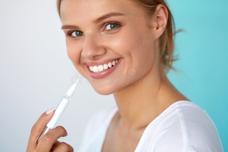 White Smile. Closeup Portrait Of Beautiful Happy Smiling Woman With Perfect Healthy White Teeth Using Teeth Whitening Pen. Dental Health And Beauty, Tooth Care Concept. High Resolution Image. White Smile. Closeup Portrait Of Beautiful Happy Smiling Woman With Perfect Healthy White Teeth Using Teeth Whitening Pen. Dental Health And Beauty, Tooth Care Concept. High Resolution Image