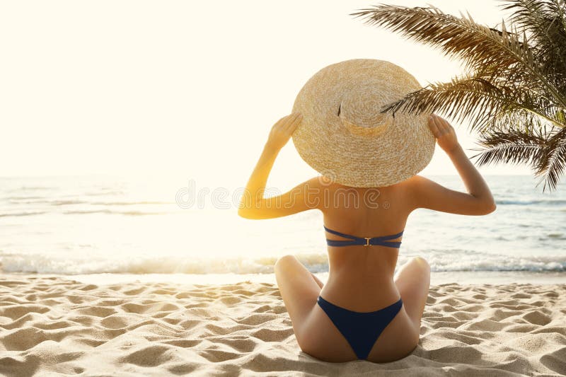 Woman Bikini Tropical Beach Back View. Beauty Model Girl in Sumer Hat Sun Tanning under Palm. Summer Beach Vacation. Holiday Sea