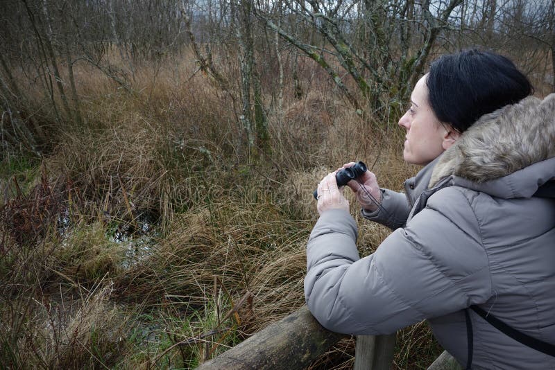 Woman with binoculars birdwatching, taking a rest on bridge