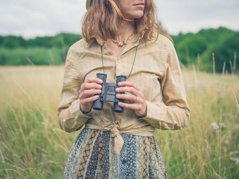 A young woman with binoculars is standing in a field in the wilderness. Adventurer adventure stock images, royalty-free photos and pictures