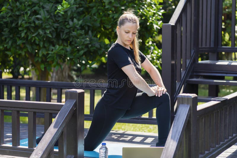 A woman in black clothes does yoga on the porch of her house. training with teachers online on the computer. yoga group sports and