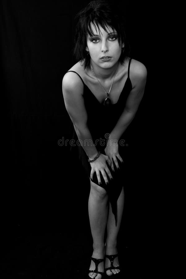 Attractive young woman in a short black evening dress, leaning forward with her hands on her thighs. Black and white photo. Isolated on black background. Attractive young woman in a short black evening dress, leaning forward with her hands on her thighs. Black and white photo. Isolated on black background.