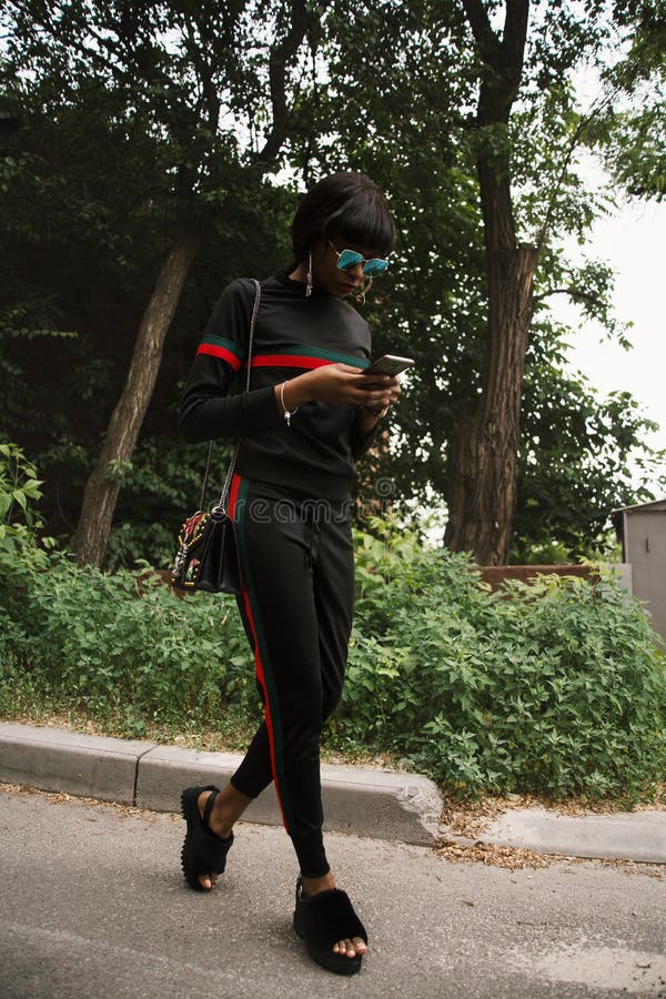 Woman In Black, Green, And Red Gucci Sweatshirt And Sweatpants Using Smartphone Picture. Image