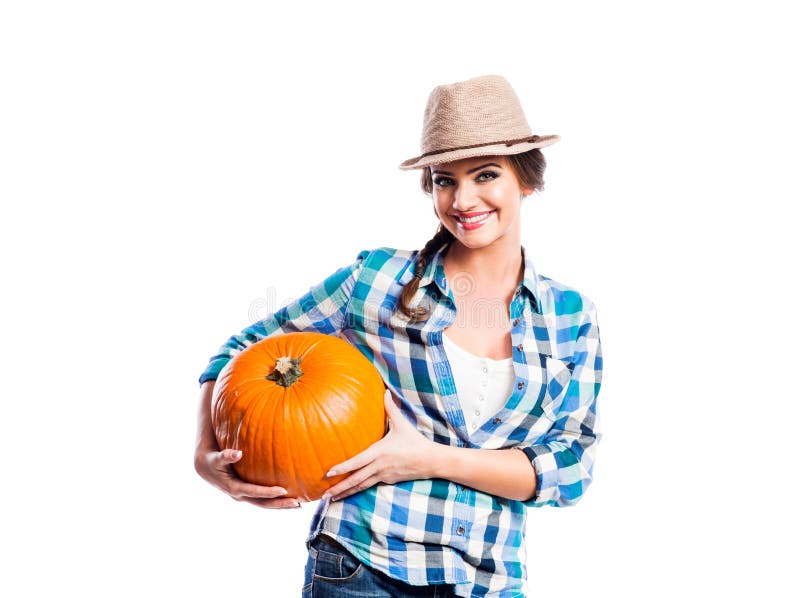 Woman in blue checked shirt, hat holding orange pumpkin