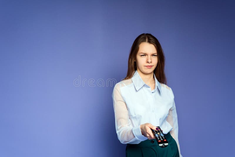 The woman in the blue shirt is disappointed and tired of the news on television. Lovely girl in the studio on a lilac background stock image The woman in the blue shirt is disappointed and tired of the news on television. Lovely girl in the studio on a lilac background stock image