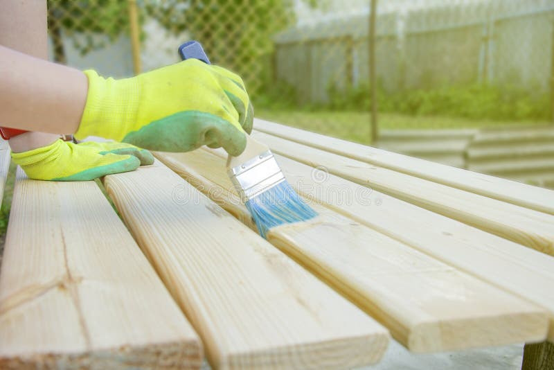 Woman with brush varnishes old wooden boards. Worker paint with brush wood wall from boards in construction site