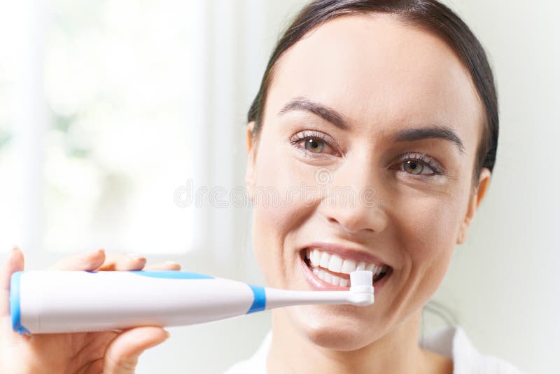 Woman Brushing Teeth with Electric Toothbrush in Bathroom Stock Image