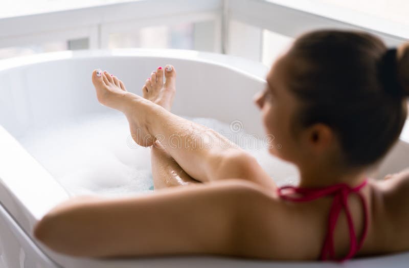 Woman in bubble bath after pedicure and toe nail polish. Lady relaxing in bathtub. Clean wet legs and feet in tub with foam.