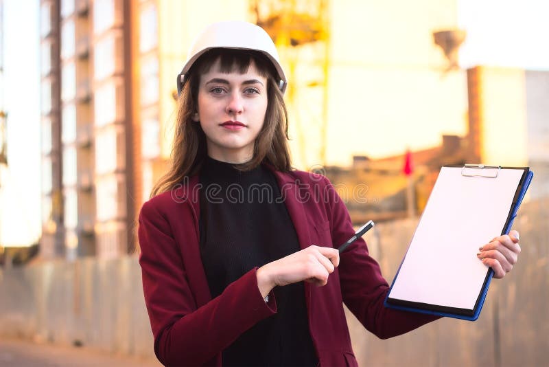 Woman builder holding blueprints, clipboard. Smiling architect girl in helmet at building background stock image Woman builder holding blueprints, clipboard. Smiling architect girl in helmet at building background stock image