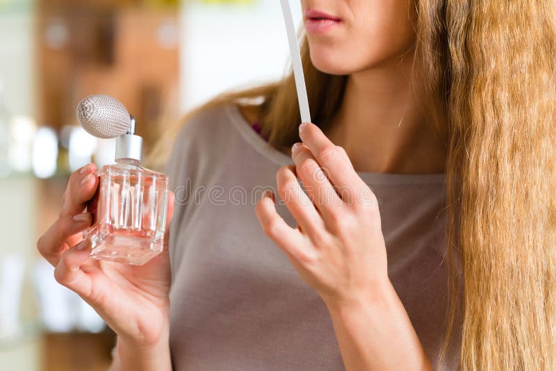 Young woman buying perfume in a shop or store, testing the fragrance with a paper tester. Young woman buying perfume in a shop or store, testing the fragrance with a paper tester