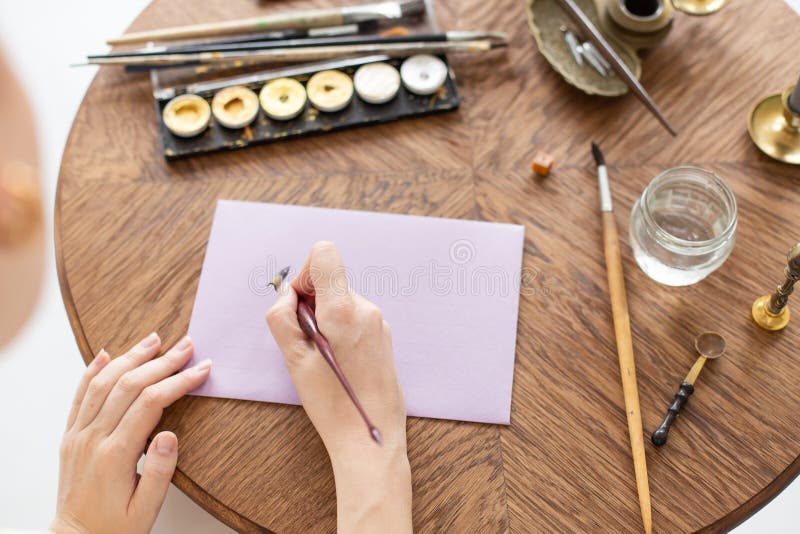 Woman calligrapher is holding a pen with ink and signs a letter in handwritten font. Close-up. Soft focus. Top view. stock photography Woman calligrapher is holding a pen with ink and signs a letter in handwritten font. Close-up. Soft focus. Top view. stock photography