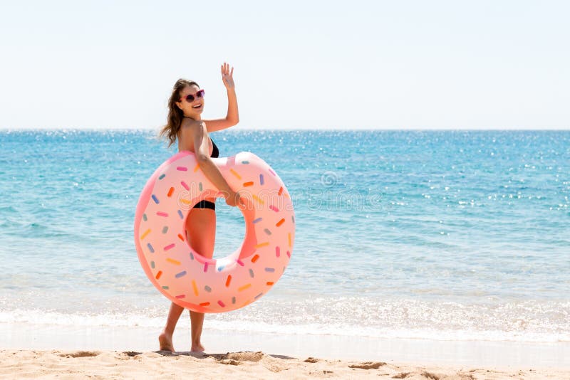 Woman calls to swim in the sea and waves her hand. Girl relaxing on inflatable ring at the beach. Summer holidays and vacation