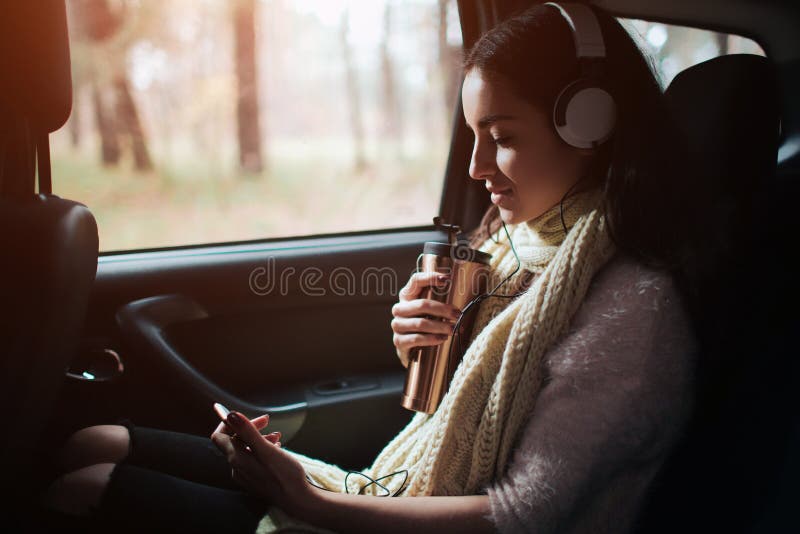 Woman in the car, autumn concept. Smiling pretty girl listening to music with headphones and reading a book moving in