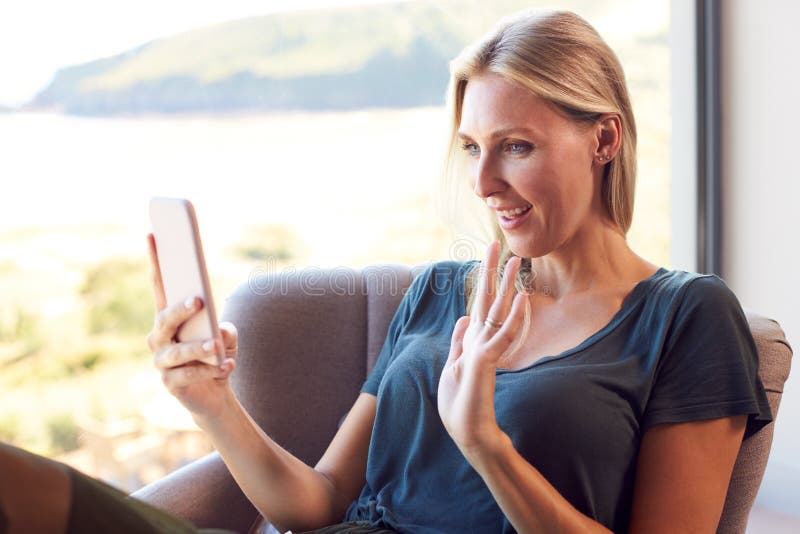 Woman In Chair By Window At Home Having Video Call On Mobile Phone stock images