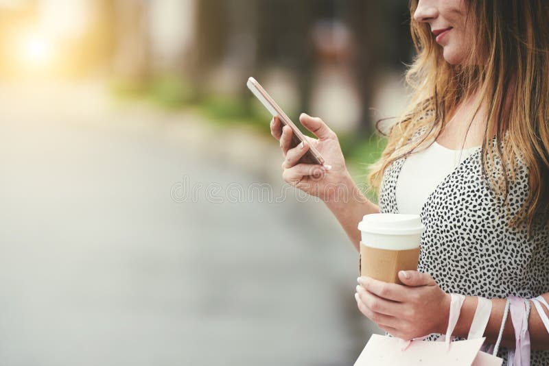 Woman checking phone. Smiling woman drinking latte and reading text messaged on her smartphone